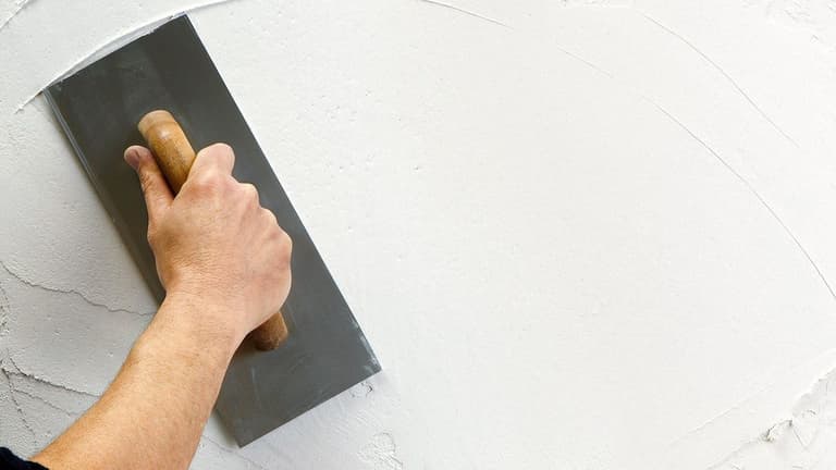 Ręka z packą szpachluje ścianę białą gładzią